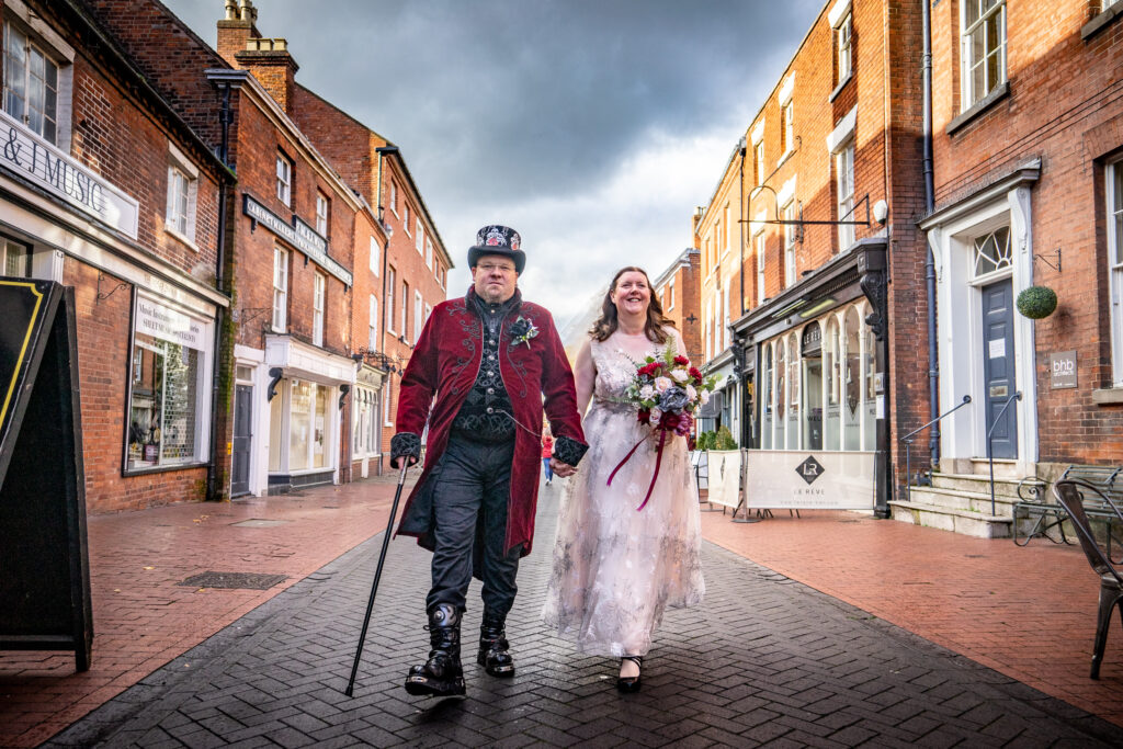 An alternative steampunk couple walk down the middle of the street from Lichfield Registry Office to their reception at The George