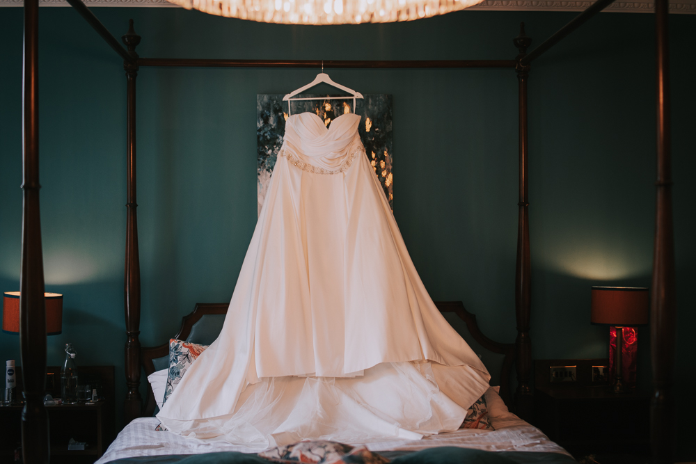 The brides dress hangs from a four poster bed against a teal wall in the bridal suite at Makeney Hall Hotel