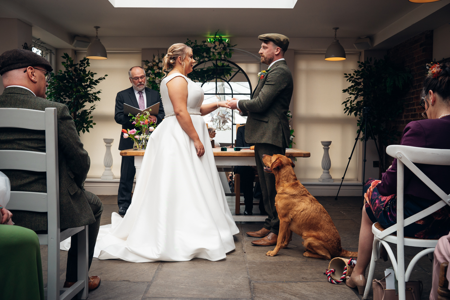 A bride, groom and their dog face each other at the head of the aisle as they are married at Kedleston Country House Hotel