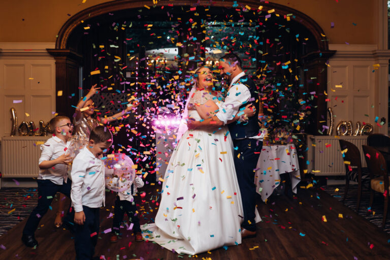 A couple look up at a mass of brightly coloured confetti falling on them as they dance their first dance at Makeney Hall Hotel