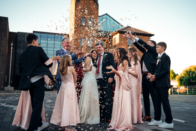 A wedding party gather around a married couple and throw confetti outside Derby Museum of Making