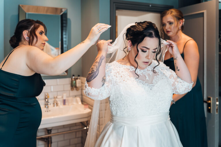 Bride adjusts her veil with bridesmaid's help as they are getting ready at The Riverside Branston