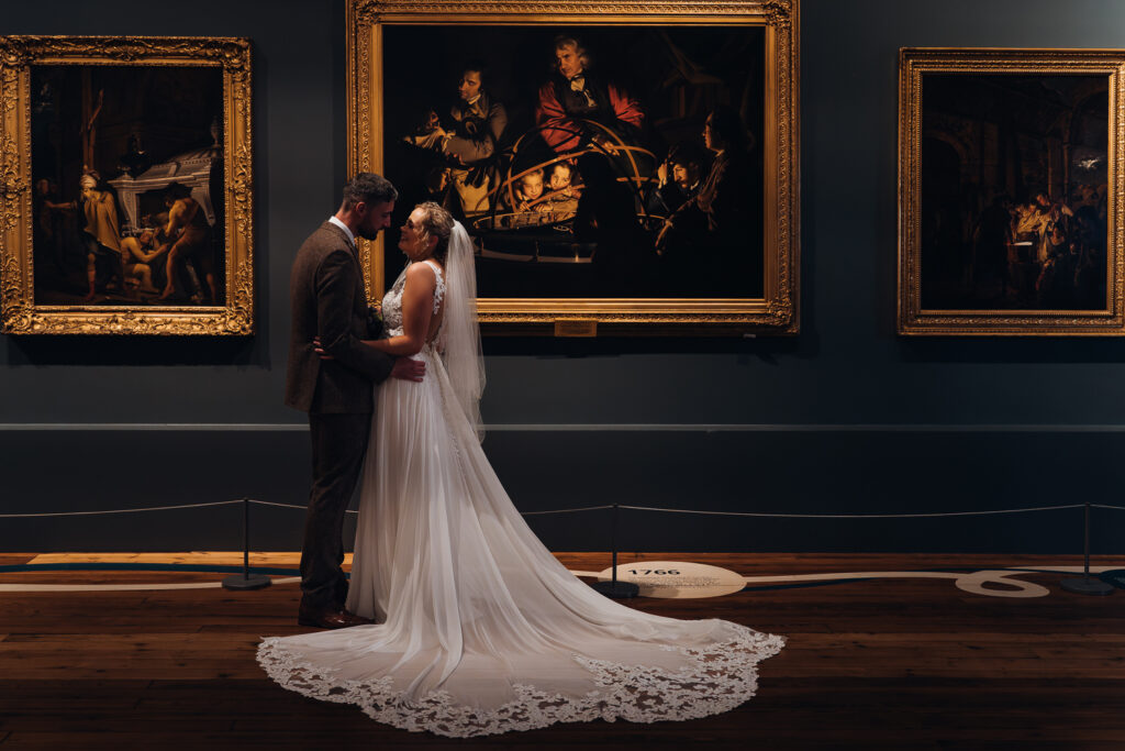 Bride and groom stand in front of Joseph Wright orrery painting at Derby Museum & Art Gallery